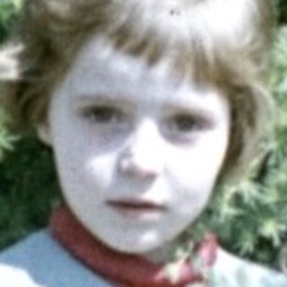 Boy standing outdoors, holding a hat, wearing a vest.