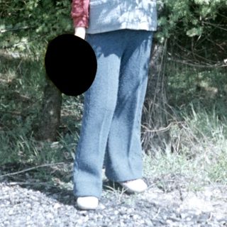 Boy standing outdoors, holding a hat, wearing a vest.