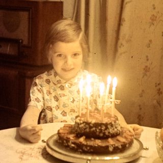 Child with birthday cake and candles at a table.