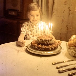 Child with birthday cake and candles at a table.