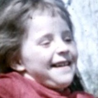 Child climbs a tree in a grassy, outdoor setting.