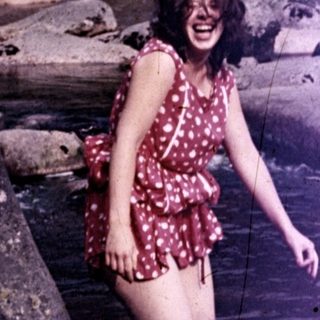 Woman wading in a rocky stream, smiling outdoors.