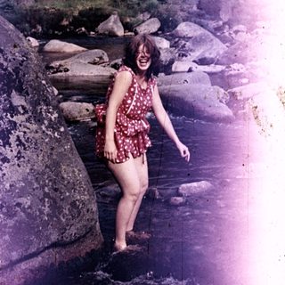 Woman wading in a rocky stream, smiling outdoors.