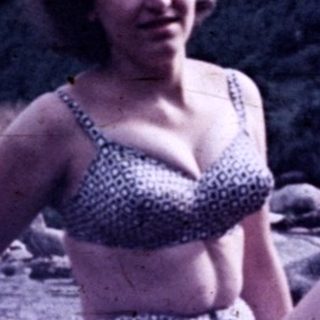 Woman in swimsuit sits on rocks by a river.
