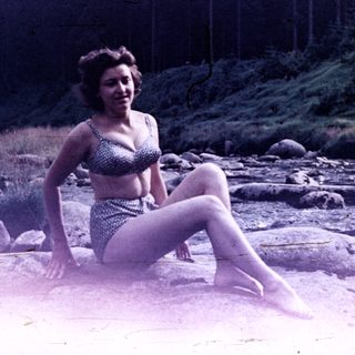 Woman in swimsuit sits on rocks by a river.