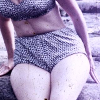 Woman in swimwear stands on rocks near a stream.