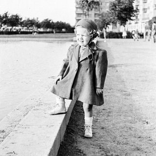 Girl in a coat stands near a waterfront ledge.