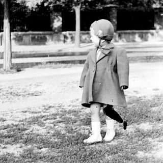 Child in coat stands on grass, looking away.