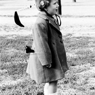 Young girl in a coat stands on a grassy area.