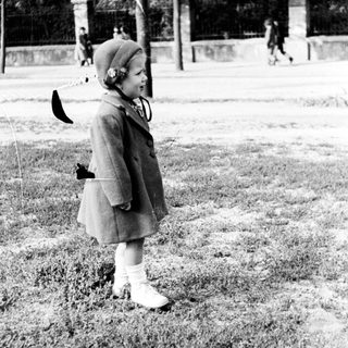 Young girl in a coat stands on a grassy area.