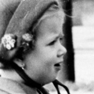 Young girl in a coat stands on a grassy area.