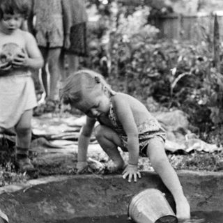 Child plays in a small pond with a bucket.