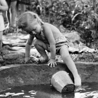 Child plays in a small pond with a bucket.