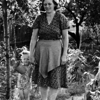Woman and child stroll through a garden scene.