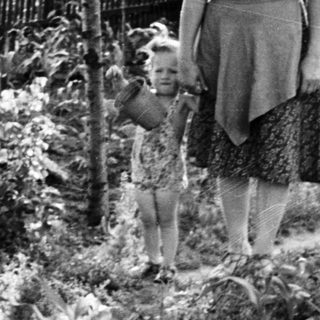 Woman and child stroll through a garden scene.