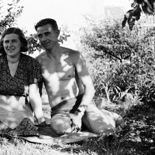 Couple sits on a blanket in a grassy area.