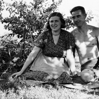 Couple sits on a blanket in a grassy area.