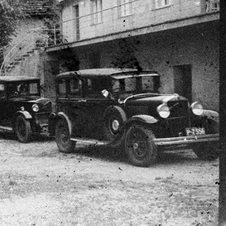 Group poses with vintage car in front of a building.