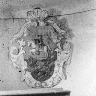 Here's a brief summary of the image: Faded, ornate coat of arms displayed on a wall.