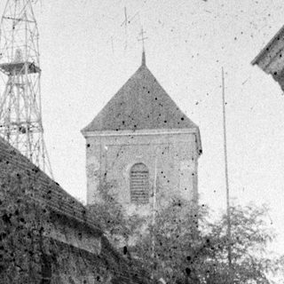 Old building with a tower and fence in background.