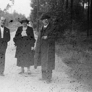 Three people standing on a dirt road in a wooded area.