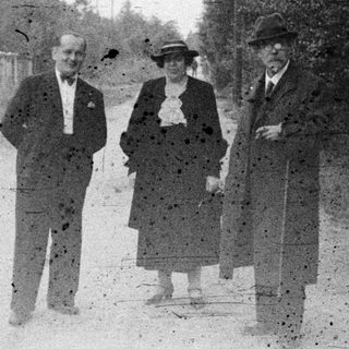 Three people standing on a dirt road in a wooded area.