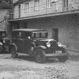 Men stand near vintage cars in front of a building.