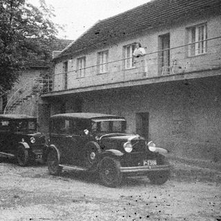Men stand near vintage cars in front of a building.