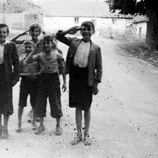 Group of children salute on a dusty road.