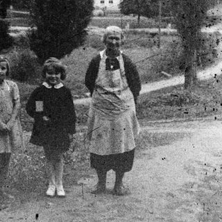 Three figures stand on a road with a house in background.