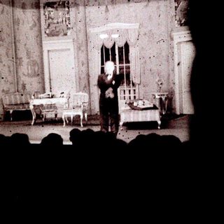 Man on stage, appearing in a staged indoor scene.
