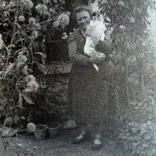 A person stands near foliage, holding a small animal.