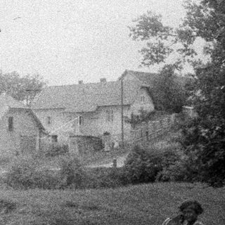 Child stands near a house with a vintage stroller.