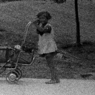 Child stands near a house with a vintage stroller.