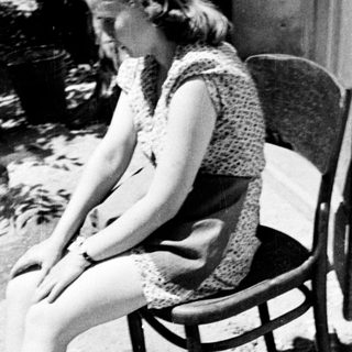 Here's a brief summary of the image: Woman sitting, soaking feet in a basin outdoors.