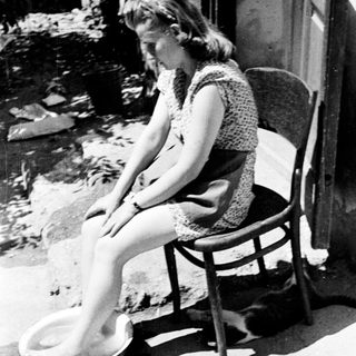 Here's a brief summary of the image: Woman sitting, soaking feet in a basin outdoors.