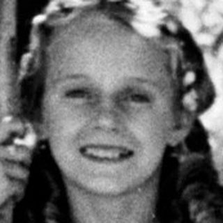 Here's a brief summary of the image: Girl in vintage dress stands near a tree.