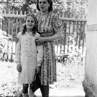 A girl and woman stand together outdoors in a vintage photo.