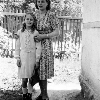 A girl and woman stand together outdoors in a vintage photo.