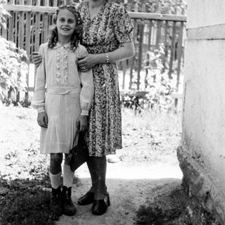 A girl and woman stand together outdoors in a vintage photo.