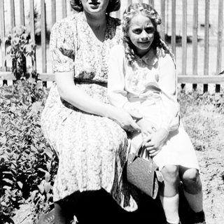 Woman and girl sit outdoors, posing for a portrait.