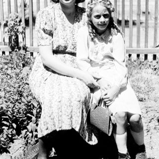 Woman and girl sit outdoors, posing for a portrait.