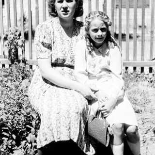 Woman and girl sit outdoors, posing for a portrait.