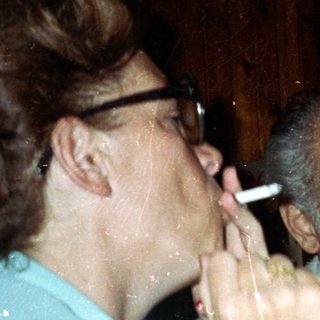 People at a table; one smokes, others drink.