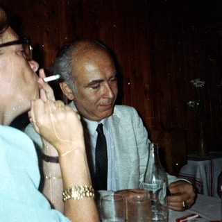 People at a table; one smokes, others drink.