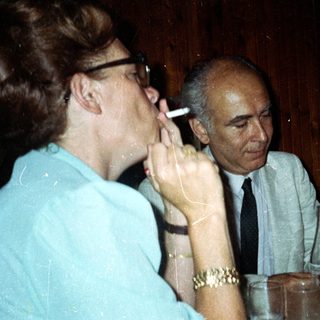 People at a table; one smokes, others drink.