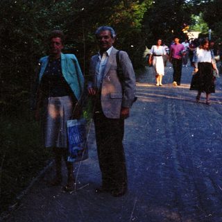 Couple stands on road with people walking in background.