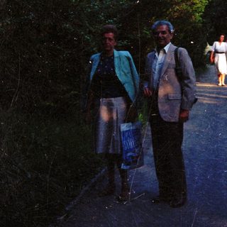 Couple stands on road with people walking in background.