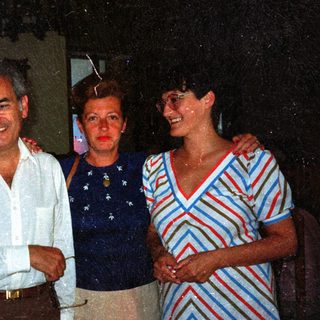 Four people standing together, smiling, in a dimly lit setting.