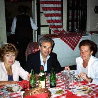 Three people dine at a table with food and drinks.